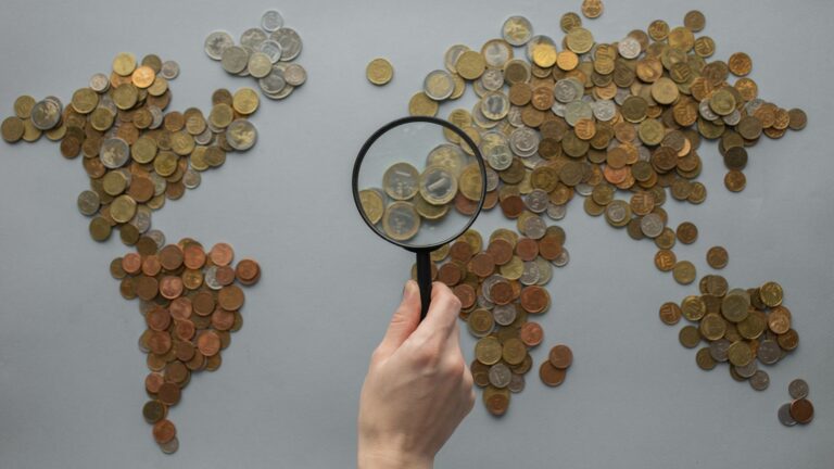 Magnifying glass held over a world map made of coins