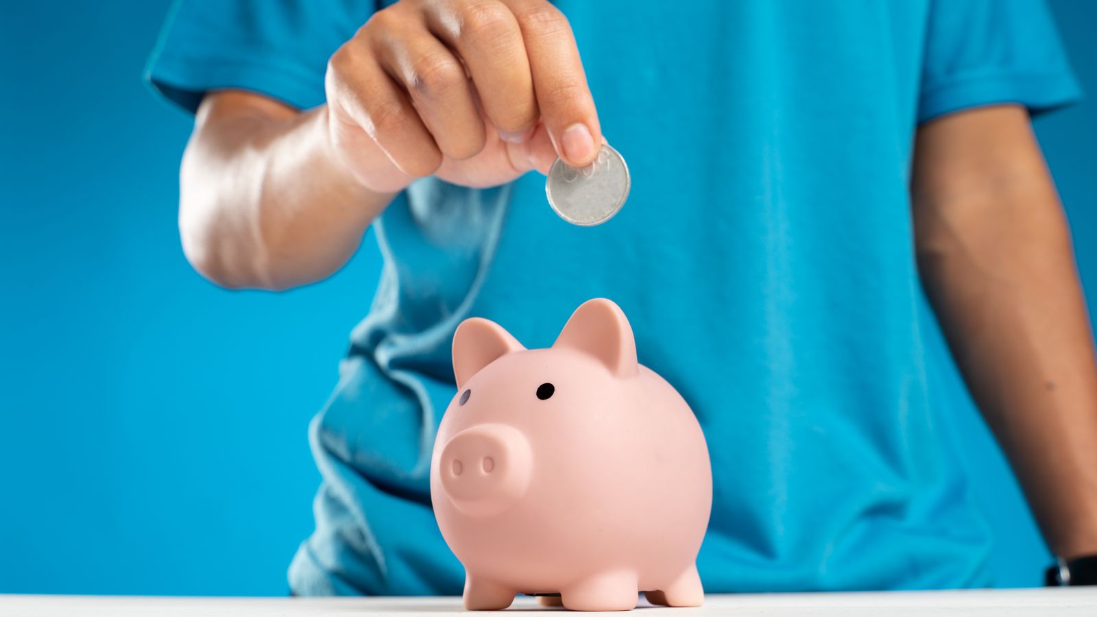 Hand placing a coin into a piggy bank